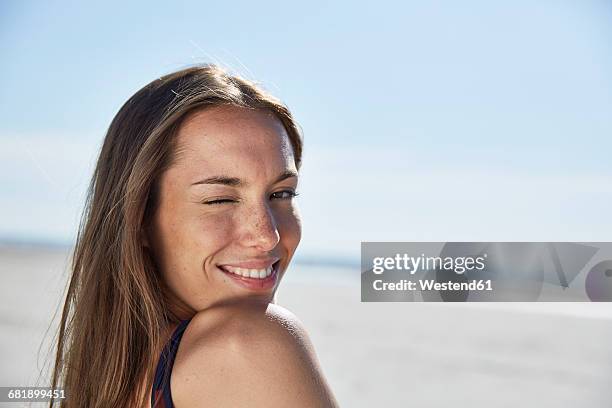 smiling young woman twinkling on the beach - winking stockfoto's en -beelden