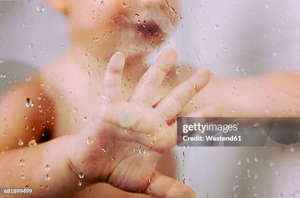 hand of little boy against wet glass pane in shower - glass of water hand ストックフォトと画像