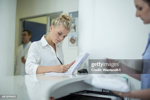 woman writing in book at reception - bata de laboratório - fotografias e filmes do acervo