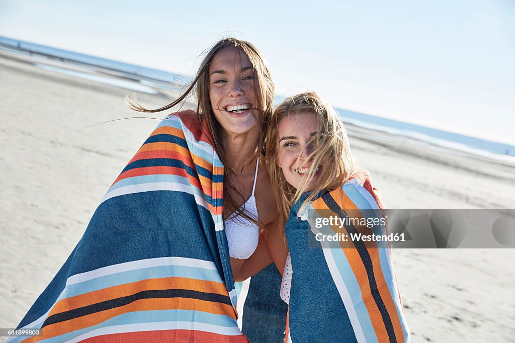 Two happy young women wrapped in a blanket on the beach