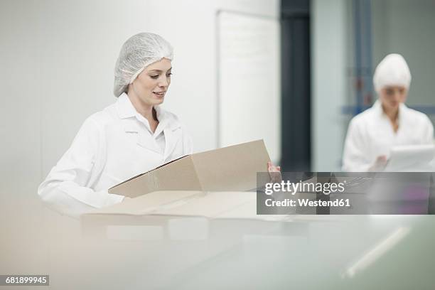 woman in protective workwear lifting cardboard box - box lifting technique stock-fotos und bilder
