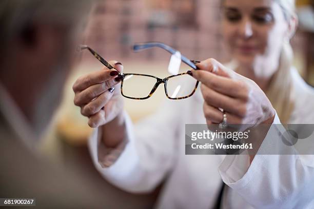 optician helping customer to choose new spectacles - opticien stockfoto's en -beelden