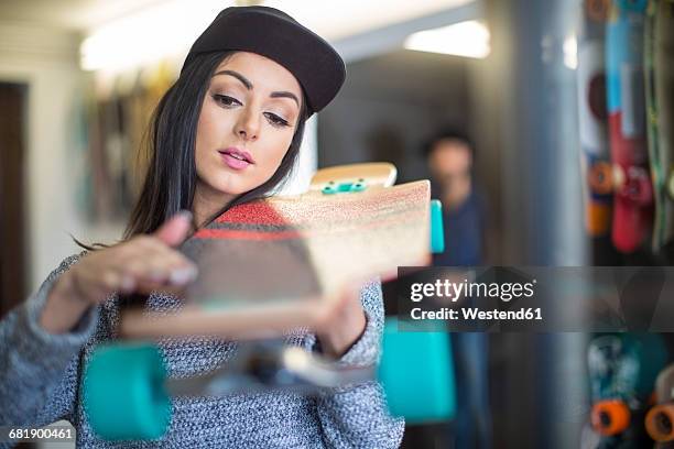 young woman examining skateboard in shop - skateboard shop stock pictures, royalty-free photos & images