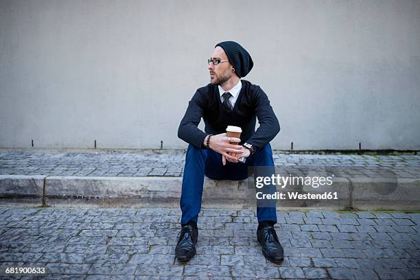 young man sitting on curb with takeaway coffee - curb 個照片及圖片檔