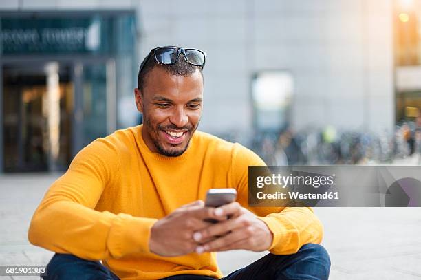 smiling man wearing yellow pullover looking at cell phone - man looking at foreground stock pictures, royalty-free photos & images