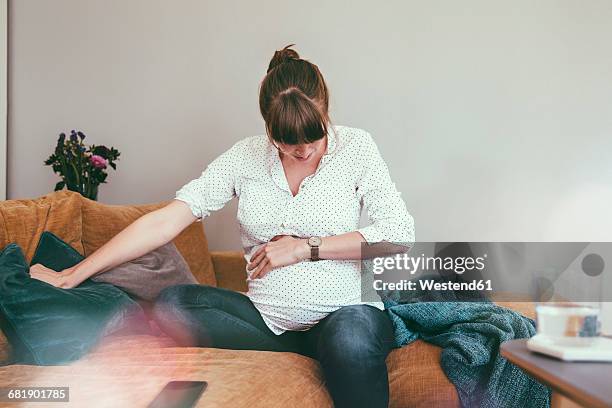 expectant mother timing her contractions while sitting on couch at home - geburt stock-fotos und bilder