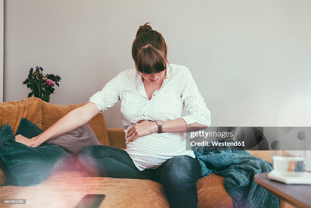 Expectant mother timing her contractions while sitting on couch at home