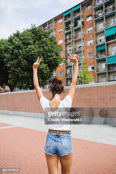 back view of young woman listening to music outdoors - women in daisy dukes stock pictures, royalty-free photos & images