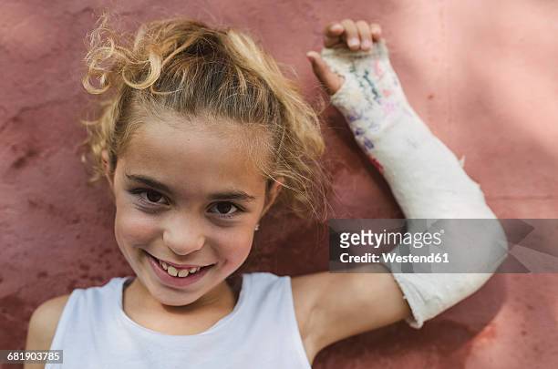 portrait of smiling blond girl with plastered arm - orthopedic cast stock-fotos und bilder