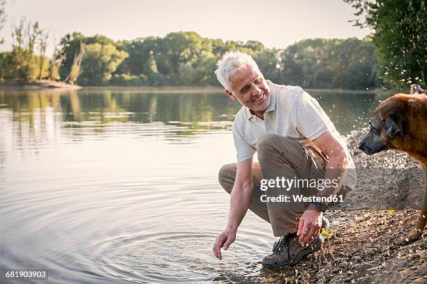 senior man playing with dog at a lake - かがむ 人 横 ストックフォトと画像