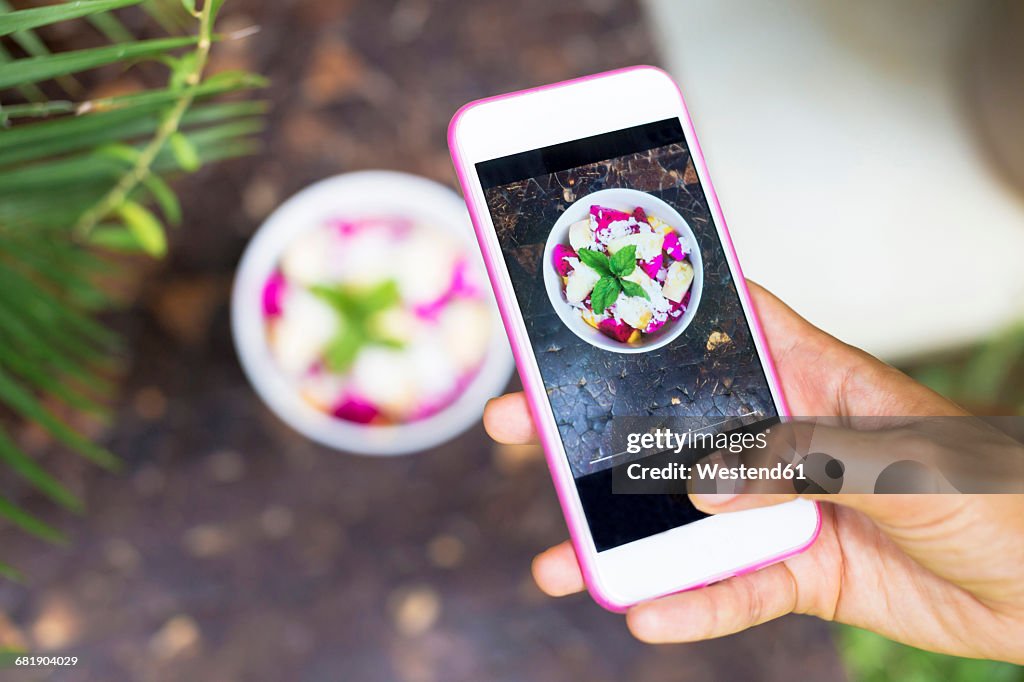 Woman taking picture of tropical fruit salad with cell phone, close-up
