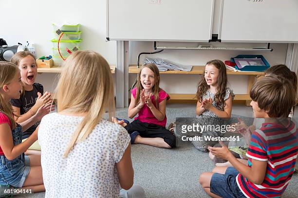 teacher and pupils sitting on floor of their classroom singing and clapping hands - enfant chant classe photos et images de collection