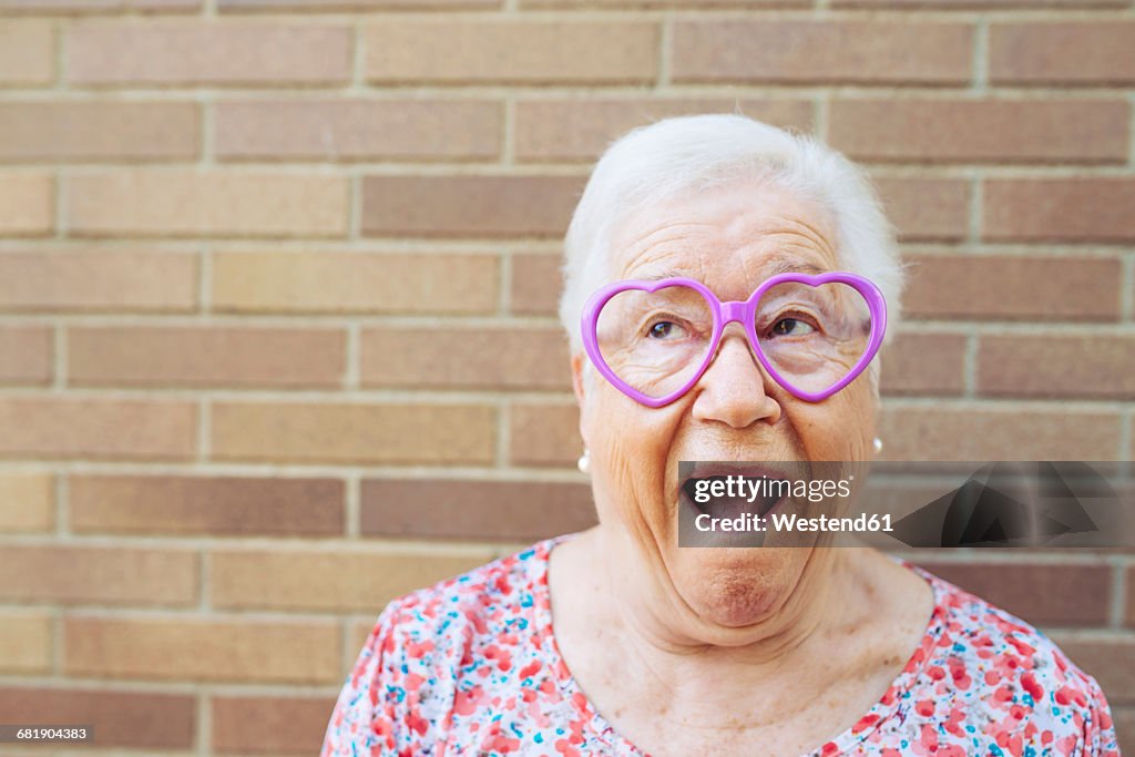 Portrait of senior woman wearing heart-shaped glasses pulling funny faces