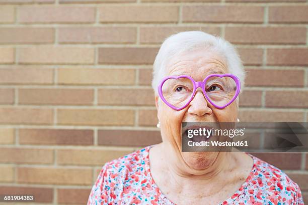 portrait of senior woman wearing heart-shaped glasses pulling funny faces - funny face woman 個照片及圖片檔