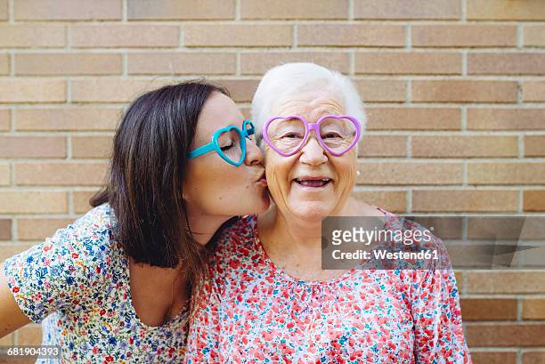 happy granddaughter and grandmother wearing heart-shaped glasses - people kissing stock pictures, royalty-free photos & images