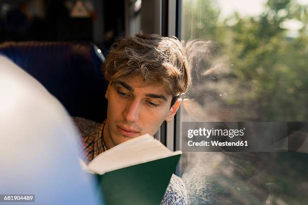 young man reading book in a train - lezen stockfoto's en -beelden