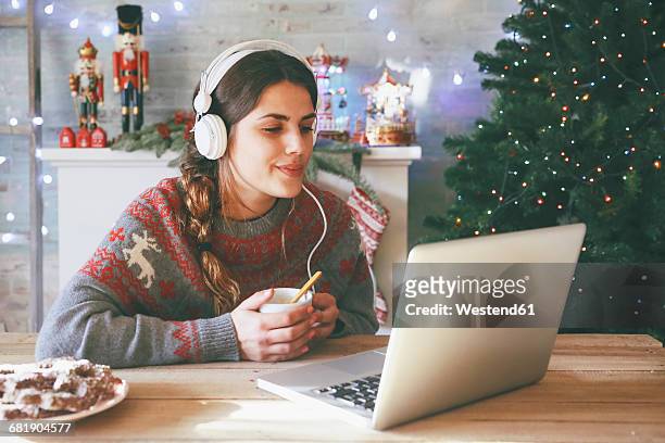 woman with cup of coffee using laptop and headphones at christmas time - weihnachten laptop stock-fotos und bilder