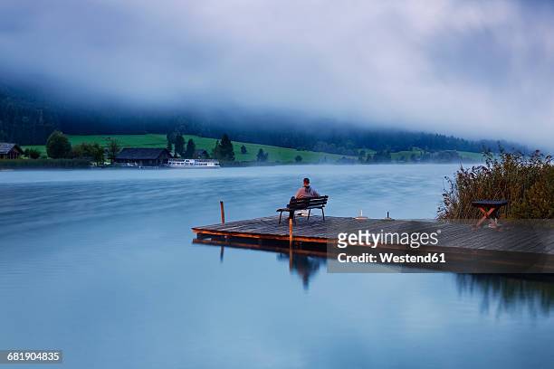 austria, carinthia, man sitting on jetty at lake weissensee - kärnten stock-fotos und bilder