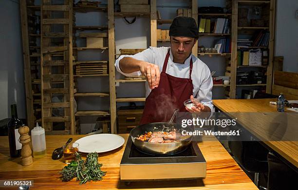man pouring salt on beef cheeks in a pan with sauteed vegetables - sal de cozinha - fotografias e filmes do acervo