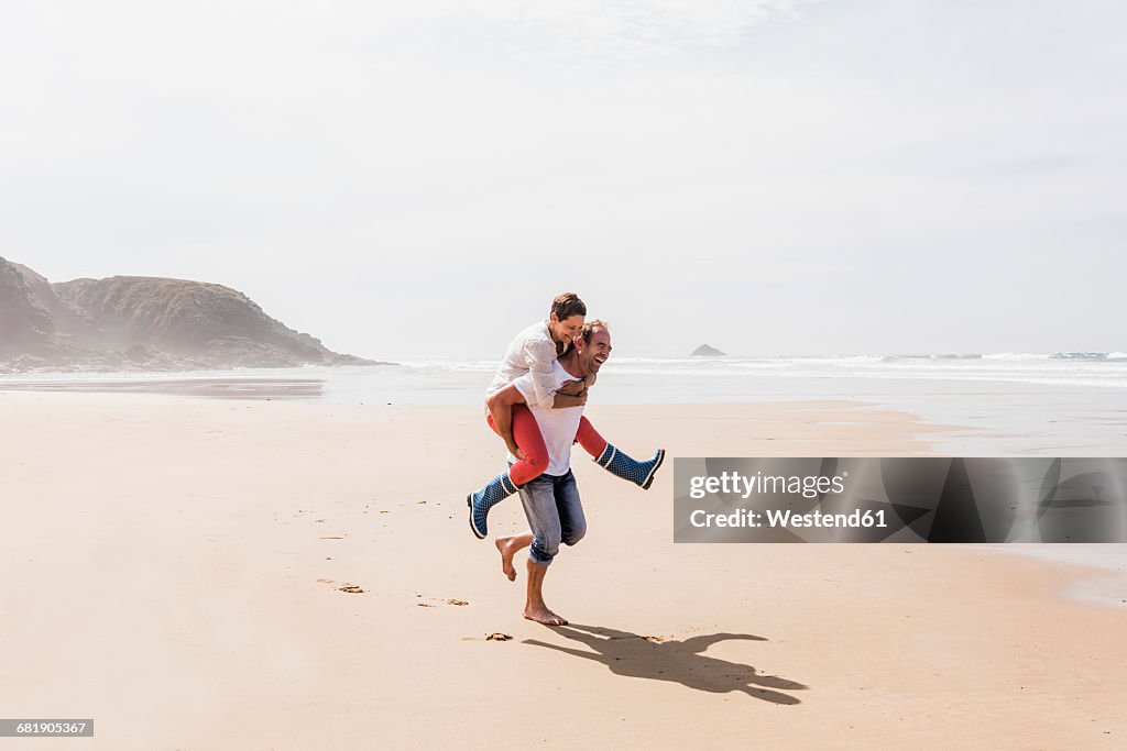 Happy mature man carrying wife piggyback on the beach