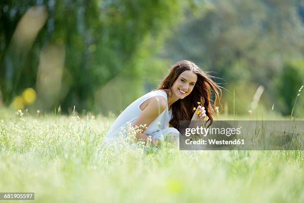 happy woman crouching on a meadow picking flowers - inclinar se pose imagens e fotografias de stock
