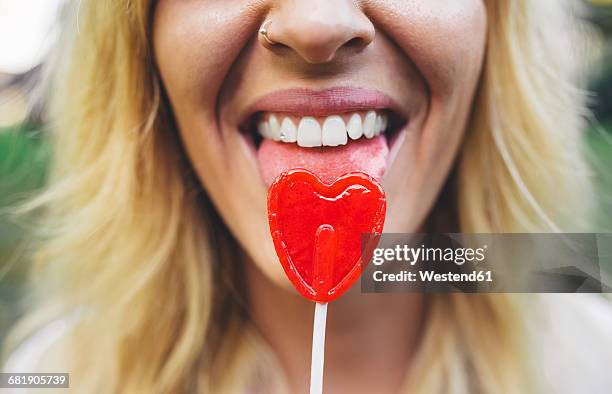 close-up of young woman licking heart-shaped lollipop - lolly stockfoto's en -beelden