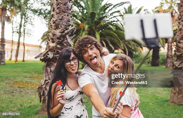 playful friends in park taking a selfie using selfie stick - candy on tongue stock pictures, royalty-free photos & images