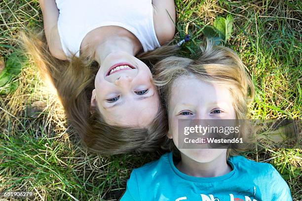 portrait of brother and little sister lying on a meadow looking up to camera - mädchen stock-fotos und bilder
