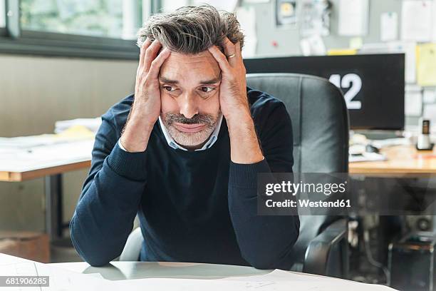 mature man sitting in office with head in hands - burn out stock-fotos und bilder