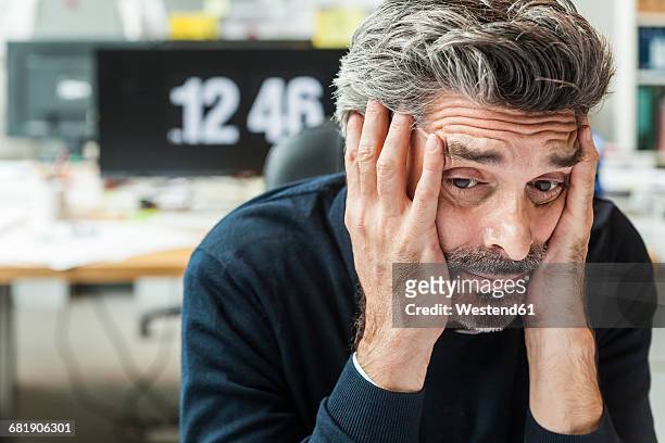 mature man sitting in office with head in hands - emotional stress stock-fotos und bilder