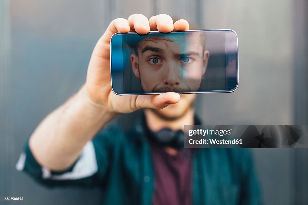 Display of smartphone showing young man pulling funny face