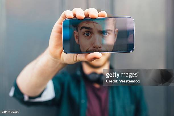 display of smartphone showing young man pulling funny face - horizontal stock-fotos und bilder
