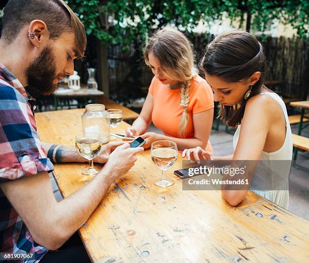 friends using cell phones and drinking spritzer at outdoor pub - heuriger stock-fotos und bilder