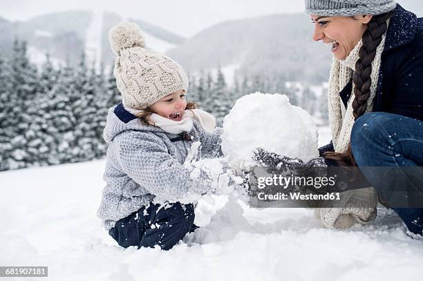 happy mother with daughter building snowman - making a snowman stock pictures, royalty-free photos & images