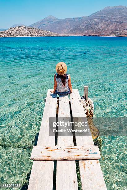 greece, cyclades islands, amorgos, woman sitting on the edge of a wooden pier, nikouria island - jetty stock pictures, royalty-free photos & images
