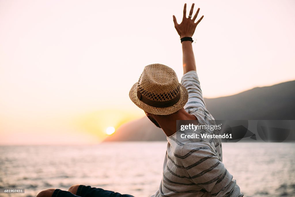 Greece, Cylcades Islands, Amorgos, man waving and enjoying the sunset next to the sea