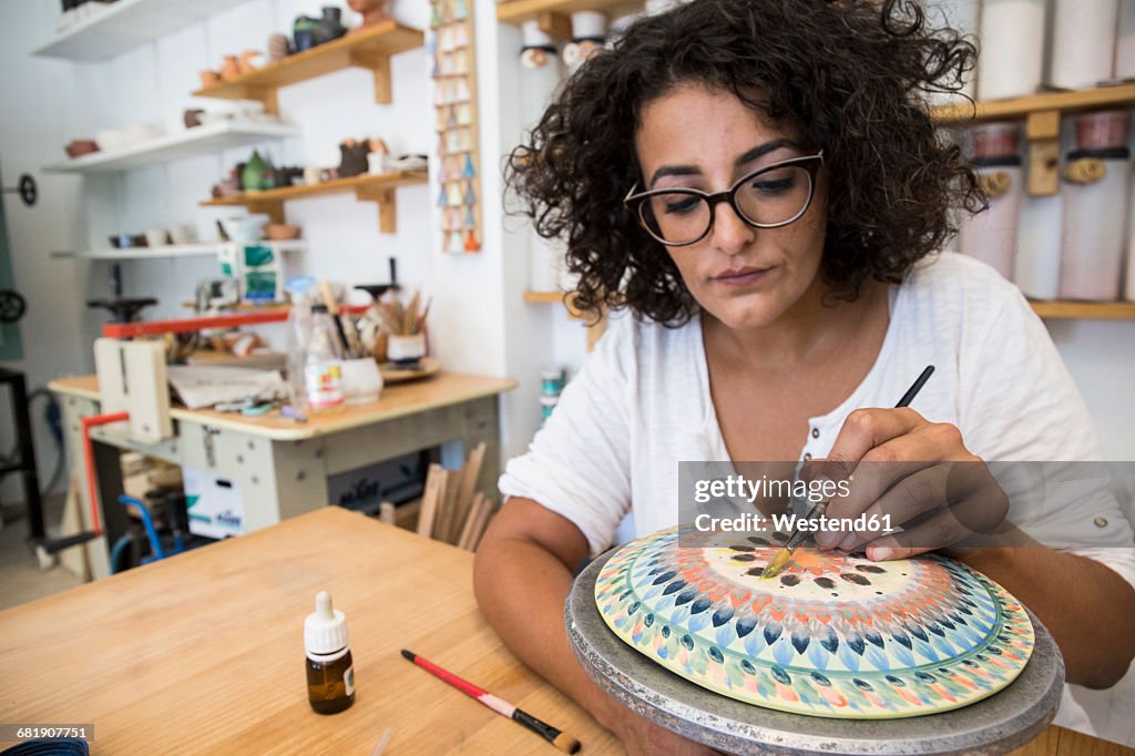 Woman painting a ceramic plate with a brush