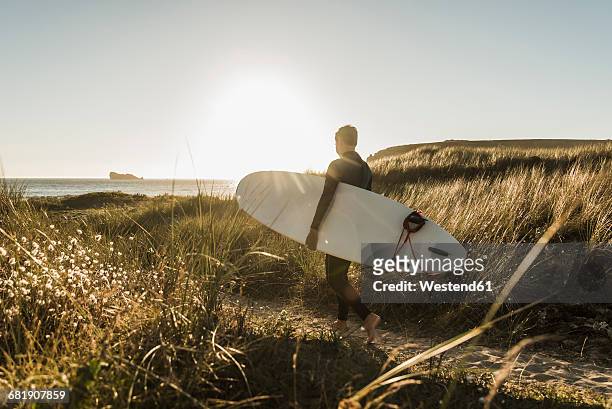 france, bretagne, crozon peninsula, woman walking through dunes carrying surfboard - surfboard photos et images de collection