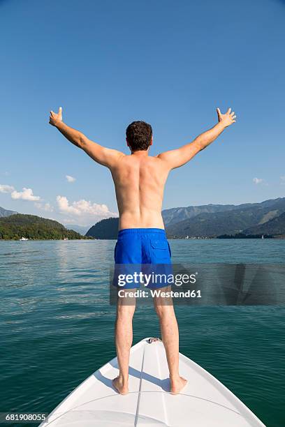 austria, sankt wolfgang, man standing on boat in lake - zwembroek stockfoto's en -beelden