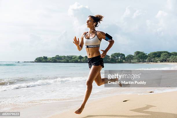 woman sprinting along beach with smart phone - gray shorts stockfoto's en -beelden