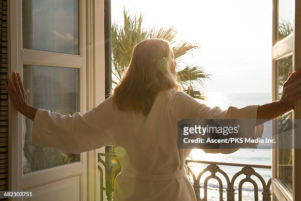 woman opens window over sea, in bath robe - travel accommodation stock pictures, royalty-free photos & images