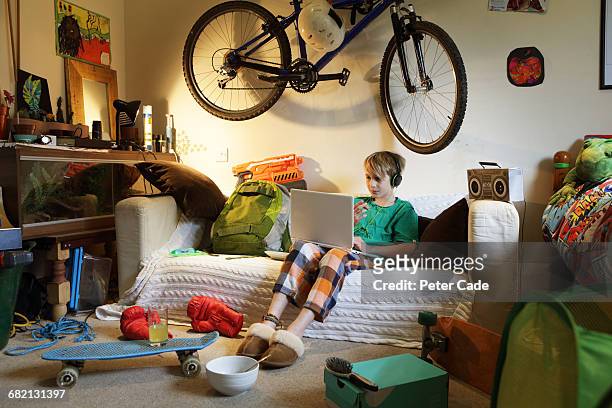 boy sat in messy bedroom looking at laptop - boy bedroom stock pictures, royalty-free photos & images