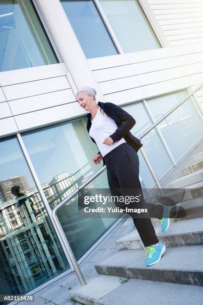 fifty year old woman jogging through a city - pants down woman fotografías e imágenes de stock