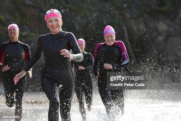 women wearing wetsuits running into sea - wetsuit stock pictures, royalty-free photos & images