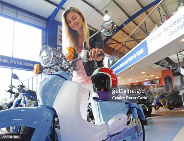 young woman stood with motorbike and helmet in showroom - buying a bike stock-fotos und bilder