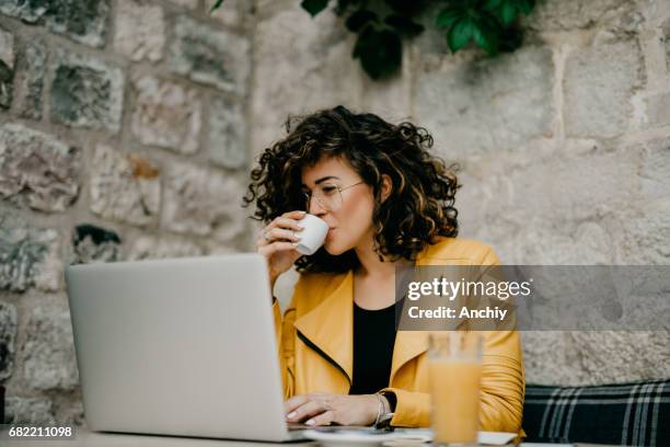 kaffeepause für eine schöne lockige mädchen - cafe laptop junge frau stock-fotos und bilder