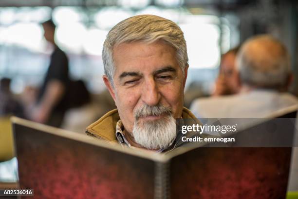 senior man reading menu in restaurant - emreogan stock pictures, royalty-free photos & images