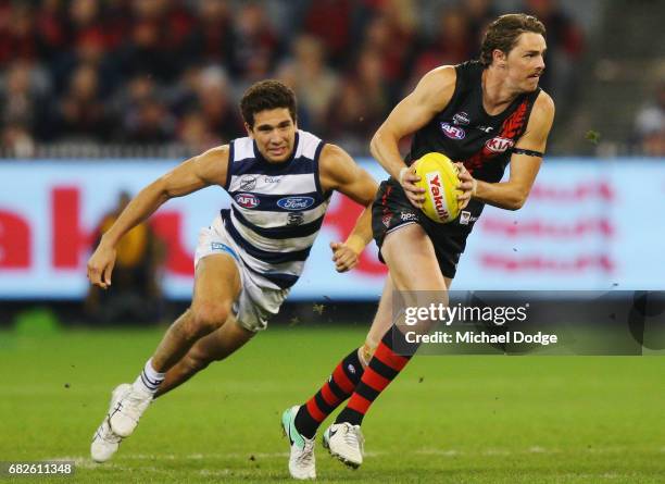 Joe Daniher of the Bombers runs with the ball away from Nakia Cockatoo of the Cats during the round eight AFL match between the Essendon Bombers and...