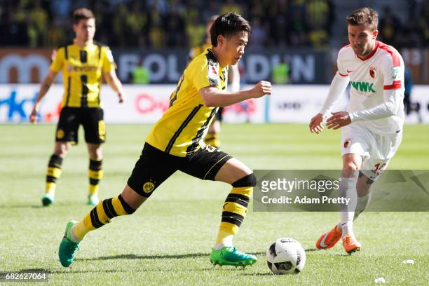 Shinji Kagawa of Borussia Dortmund is challenged by Daniel Baier of Augsburg during the Bundesliga match between FC Augsburg and Borussia Dortmund at...