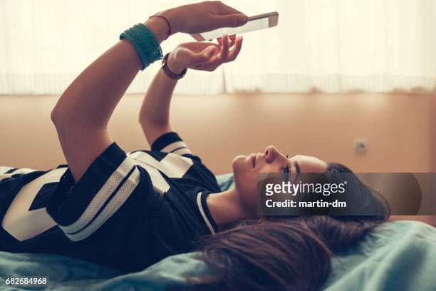 relaxed teenage girl in bed using smartphone - american football uniform stock pictures, royalty-free photos & images